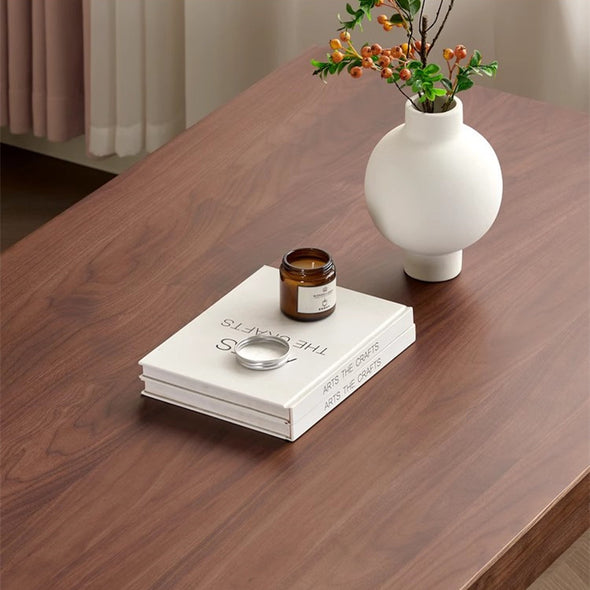 White vase with greenery on a wooden table with books and a candle